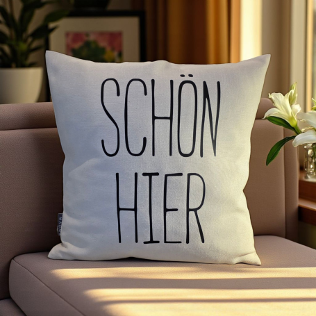 Kissen mit dem Text "SCHÖN HIER" auf einem Sofa in einem hellen Raum.
